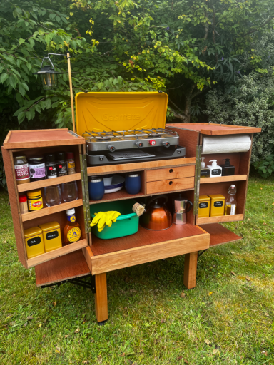 What we pack Wooden garden cart with shelves, containing tools, cans, and gardening supplies.